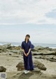 A woman in a blue dress standing on a rocky beach.