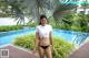 A woman in a white shirt and black bikini standing by a pool.