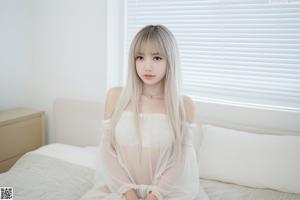 A woman sitting on a bed in a white dress.