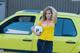 A woman holding a soccer ball in front of a yellow car.